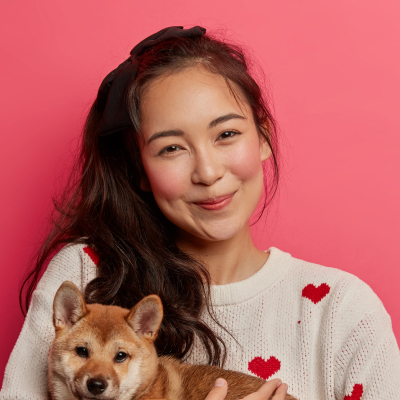 smiling woman holding corgi puppy in pink background